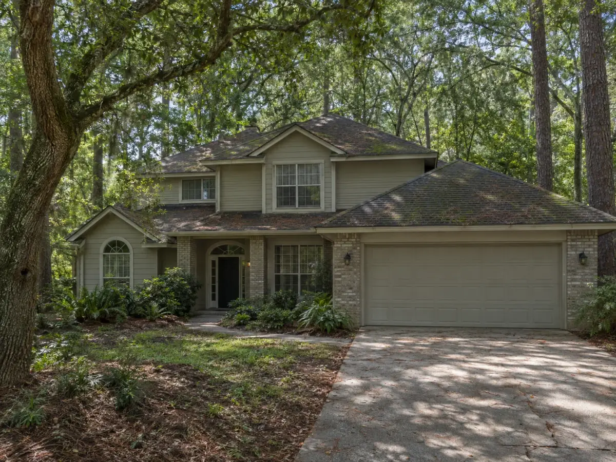 Mold remediation in Oviedo, FL · illustrative image of two-story home on a wooded lot with algae on a shaded shingle roof